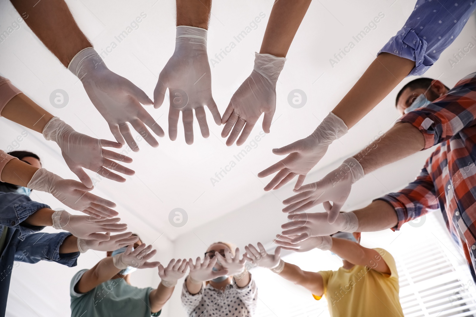 Photo of People in white medical gloves joining hands on light background, low angle view