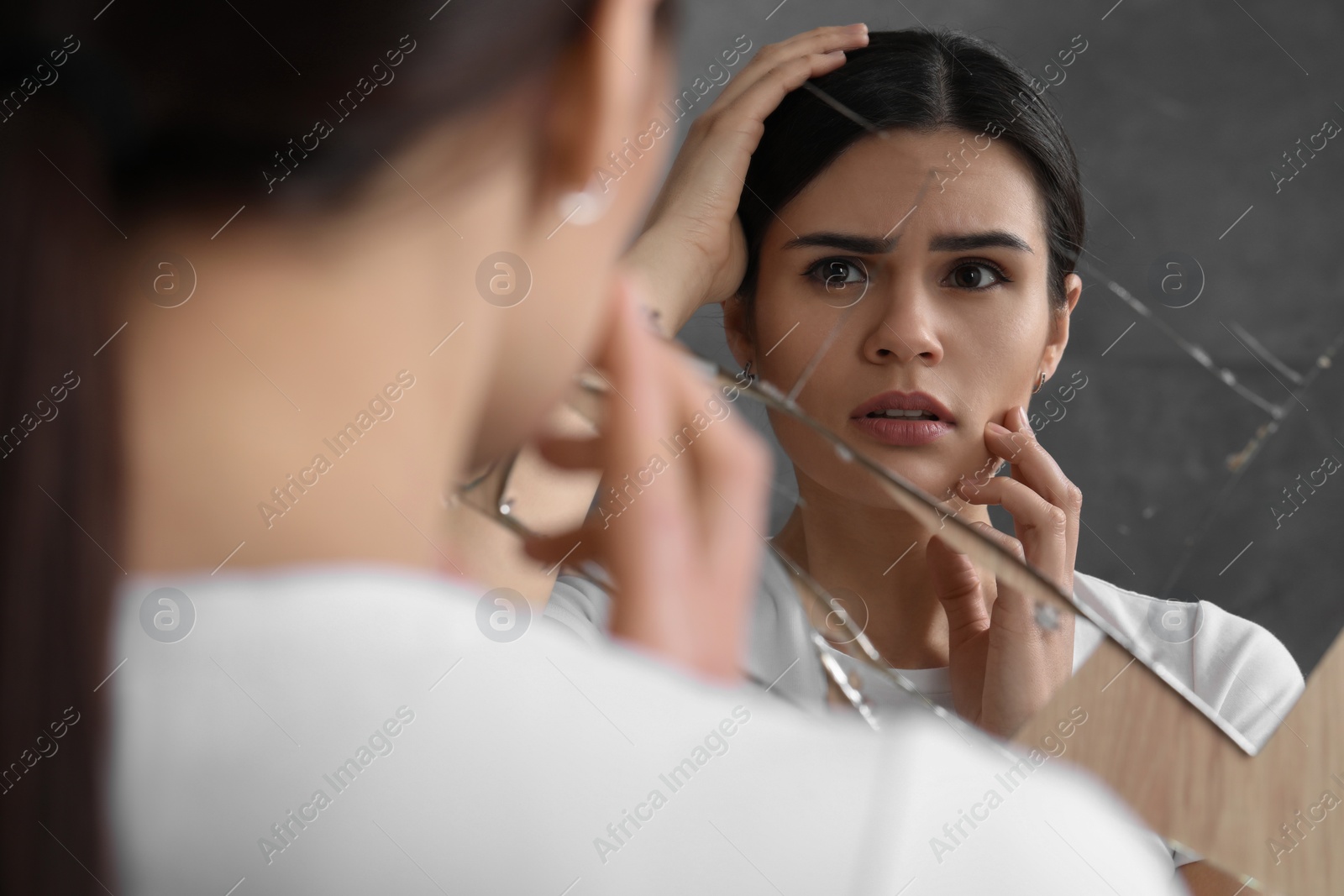 Photo of Young woman suffering from mental problems near broken mirror indoors
