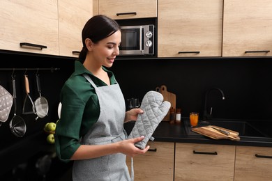 Photo of Woman in apron holding oven glove indoors