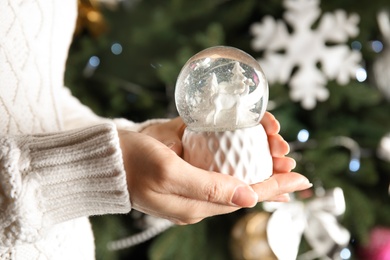 Woman holding snow globe near Christmas tree, closeup