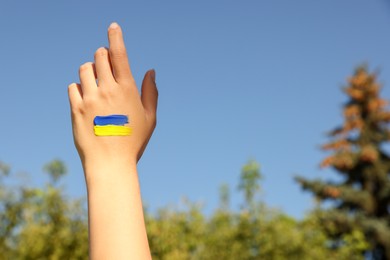 Photo of Woman with drawing of Ukrainian flag on hand outdoors, closeup. Space for text