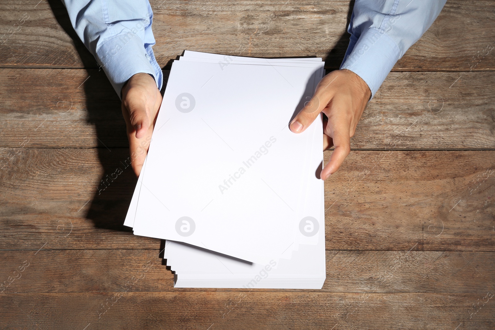 Photo of Man holding blank paper sheets for brochure at wooden table, top view. Mock up