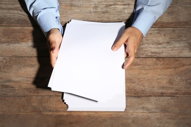 Man holding blank paper sheets for brochure at wooden table, top view. Mock up