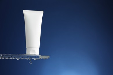 Moisturizing cream in tube on glass with water drops against blue background. Space for text