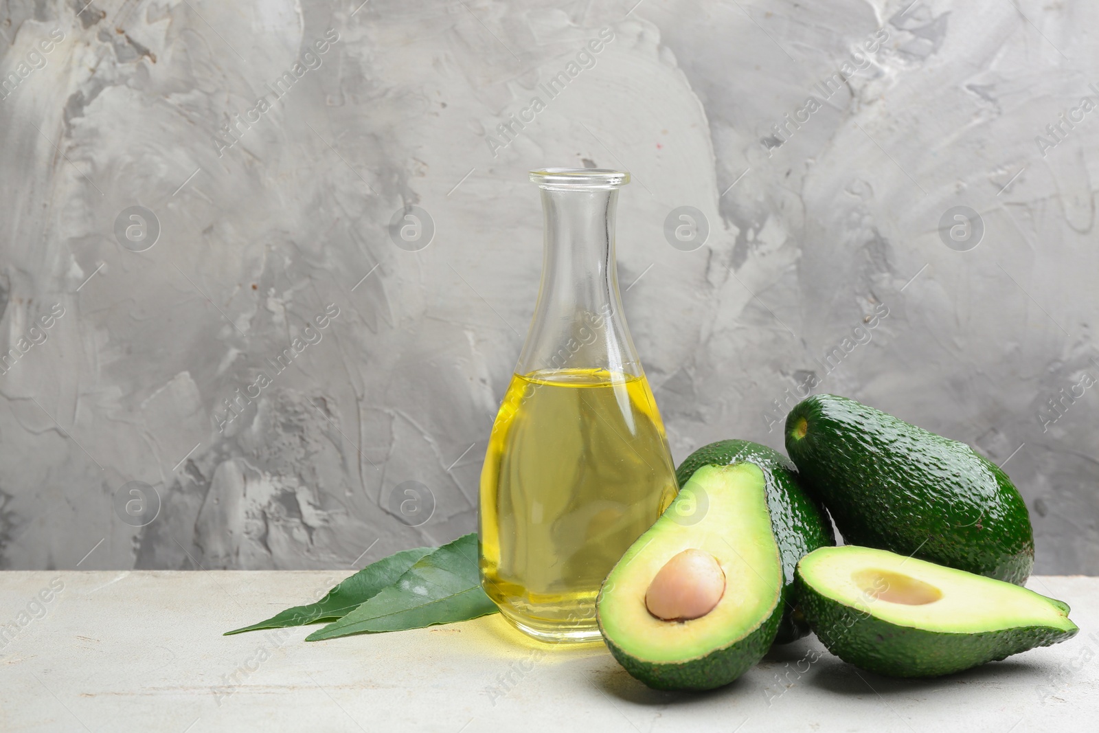 Photo of Bottle of natural oil and avocados on table against grey stone background. Space for text