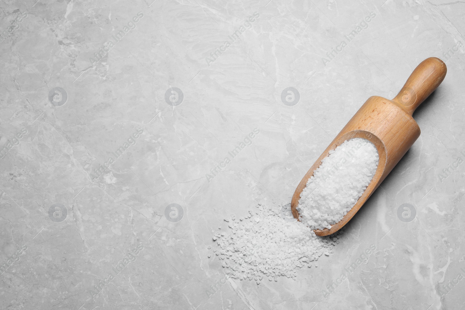 Photo of Wooden scoop and heap of natural sea salt on grey table, top view. Space for text