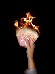 Image of Woman holding burning euro banknotes on black background, closeup