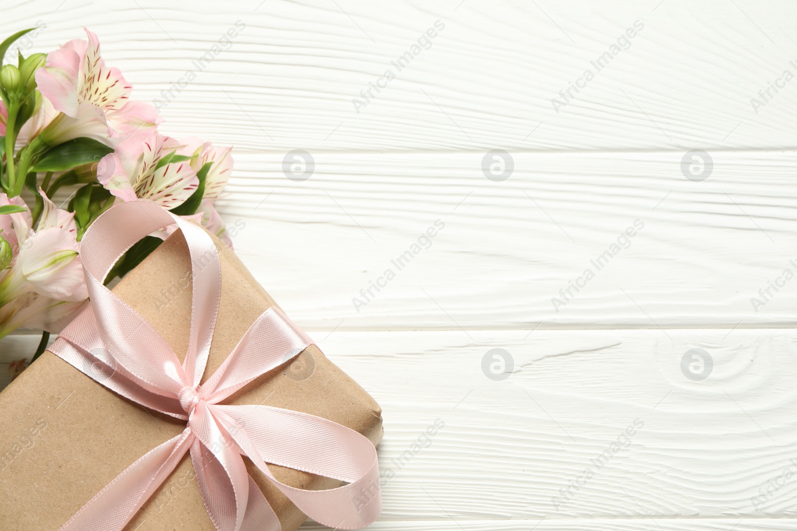 Photo of Happy Mother's Day. Beautiful flowers and gift box on white wooden table, flat lay. Space for text