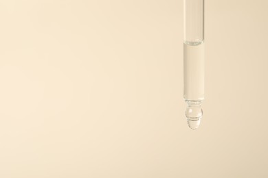 Dripping cosmetic serum from pipette on beige background, space for text