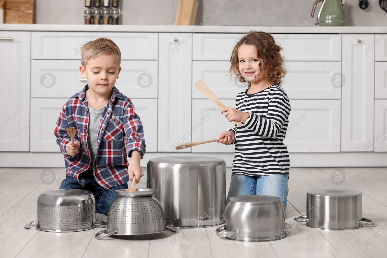 Photo of Little children pretending to play drums on pots in kitchen