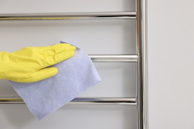 Woman cleaning heated towel rail with rag indoors, closeup