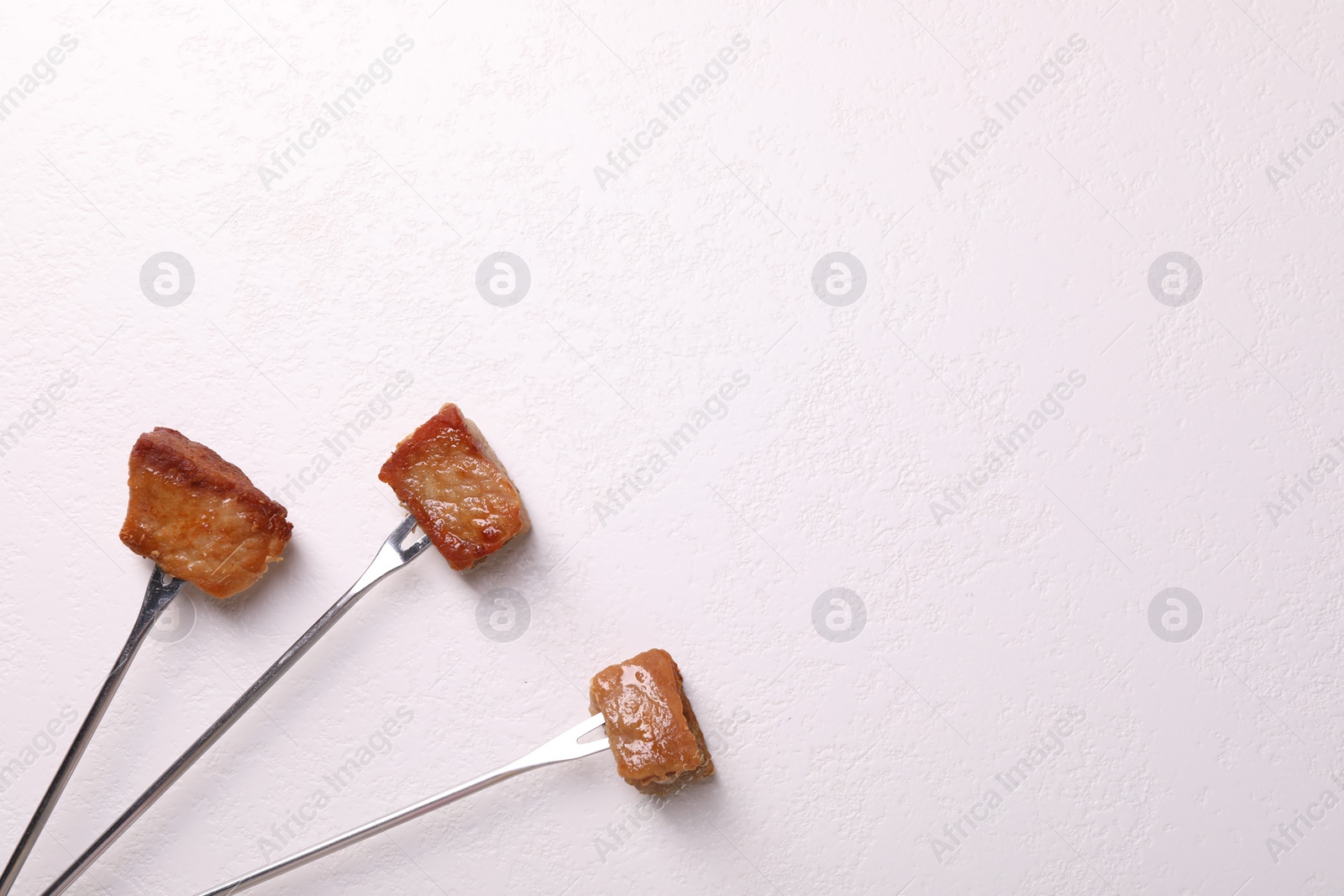 Photo of Fondue forks with pieces of fried meat on white textured table, flat lay. Space for text