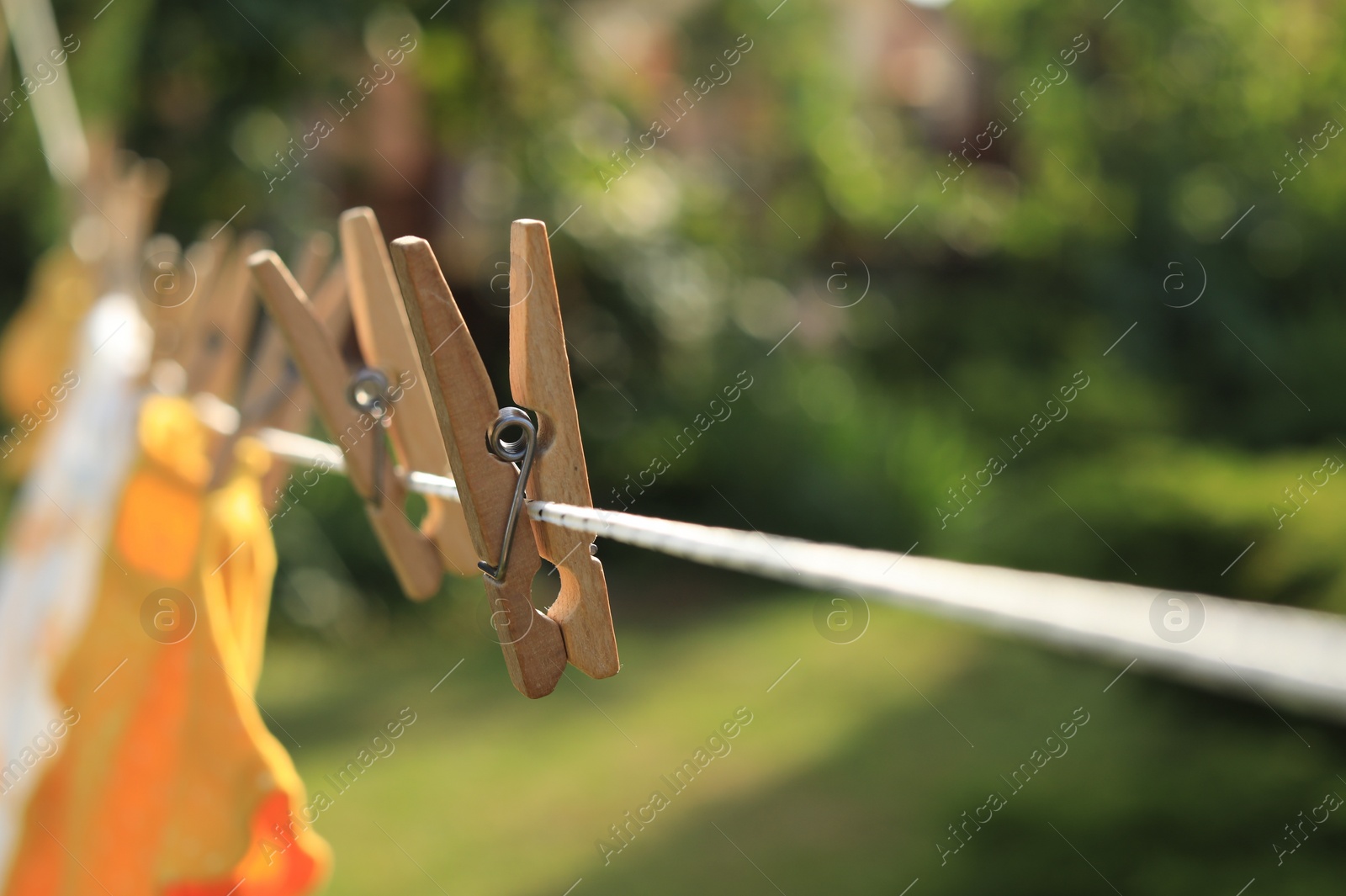 Photo of Clean clothes drying outdoors during sunny day, focus on laundry line with wooden clothespins