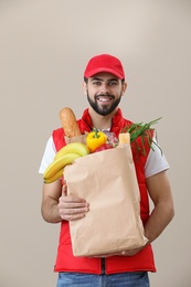 Man holding paper bag with fresh products on color background. Food delivery service