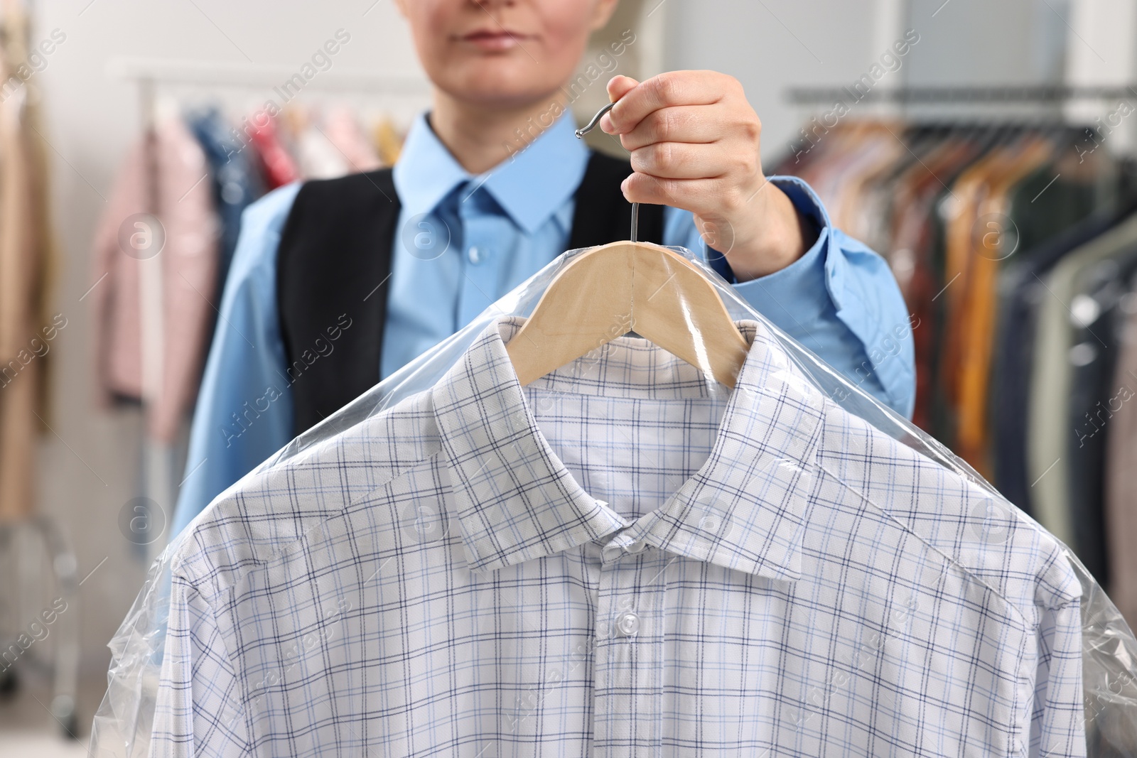 Photo of Dry-cleaning service. Woman holding shirt in plastic bag indoors, closeup