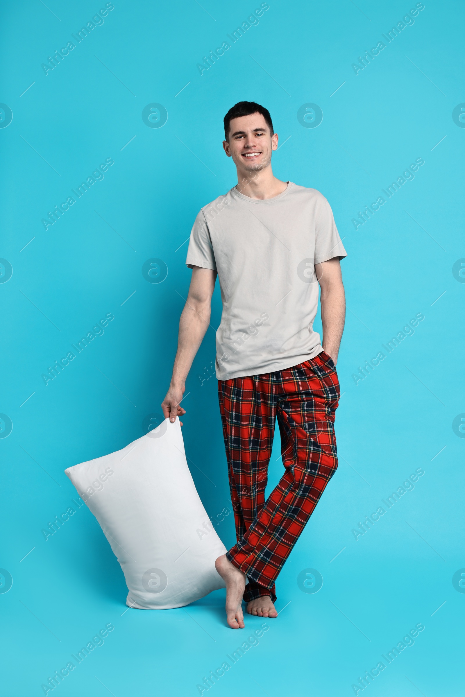 Photo of Happy man in pyjama holding pillow on light blue background