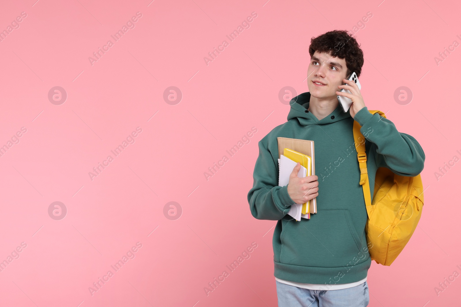 Photo of Portrait of student with backpack and notebooks talking on phone against pink background. Space for text