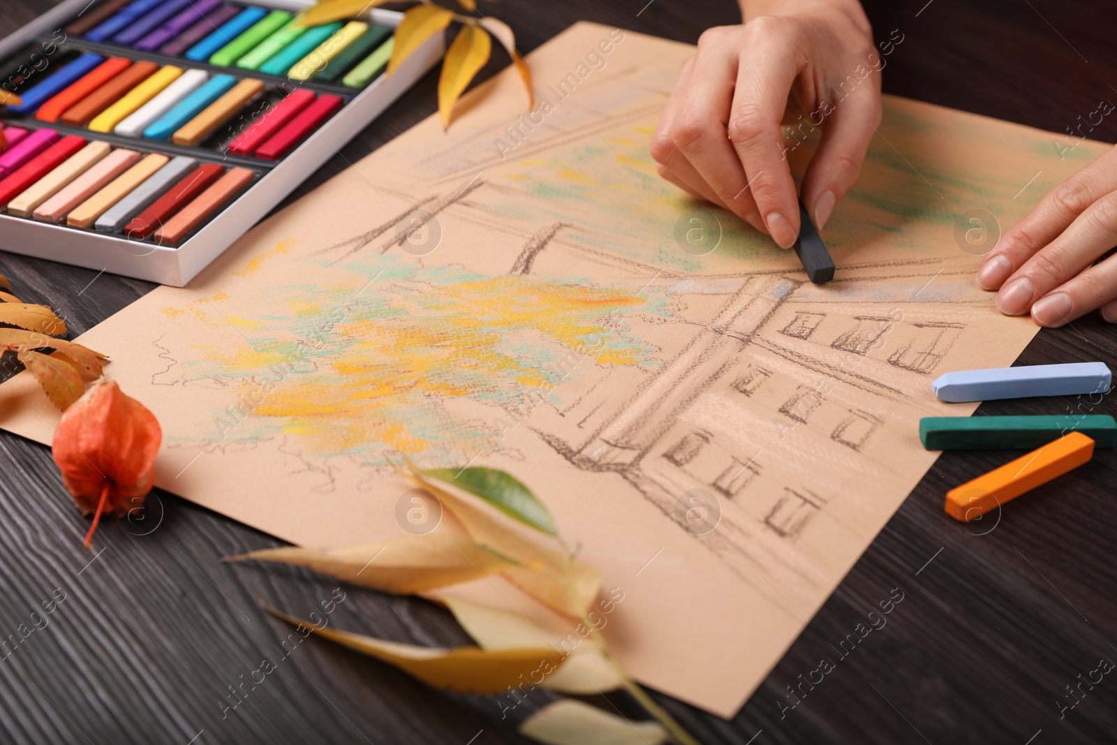 Photo of Woman drawing beautiful building with soft pastel at wooden table, closeup