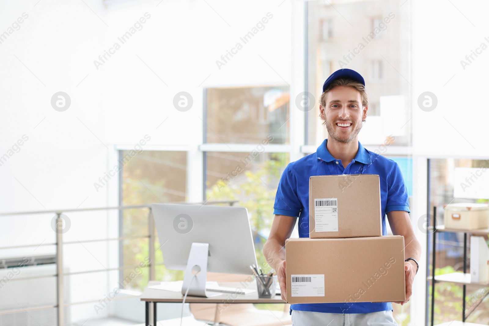 Photo of Young courier standing with parcels near office desk. Space for text