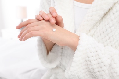 Young woman applying cream on her hands indoors, closeup. Beauty and body care