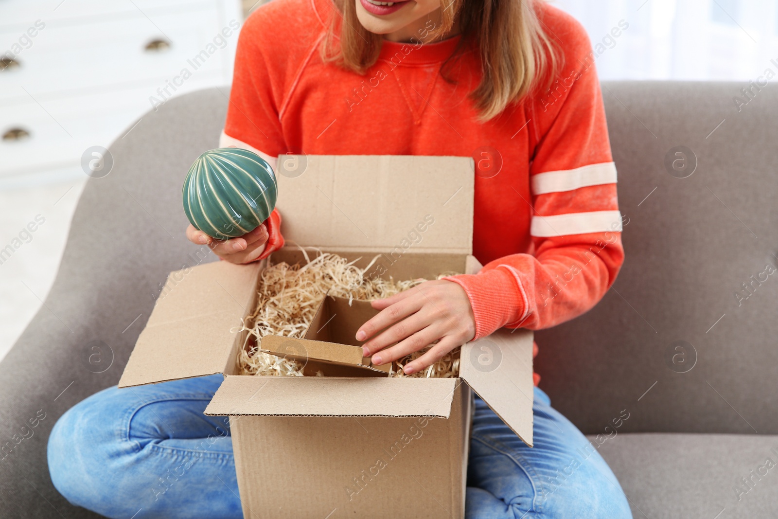 Photo of Young woman opening parcel on sofa in living room, closeup