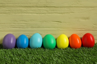 Photo of Bright Easter eggs on green grass against yellow wooden background
