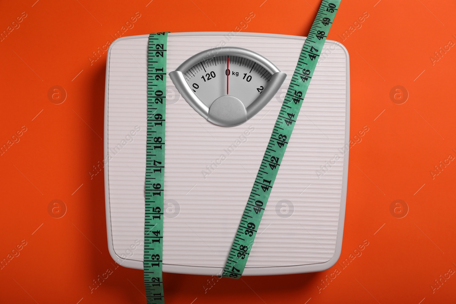 Photo of Scales and measuring tape on orange background, top view. Weight loss concept
