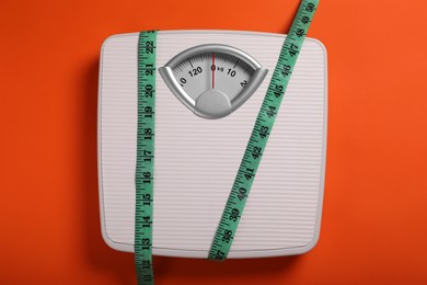 Scales and measuring tape on orange background, top view. Weight loss concept