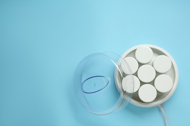 Modern yogurt maker with jars on light blue background, top view. Space for text