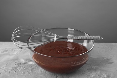 Photo of Whisk and bowl with chocolate cream on table against grey background