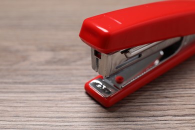 Photo of Red stapler on wooden table, closeup. Space for text