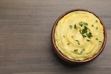 Photo of Bowl of freshly cooked mashed potatoes with parsley on wooden table, top view. Space for text