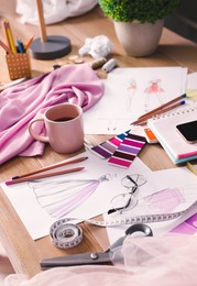 Photo of Sketches of clothes and different stuff on wooden table. Fashion designer's workplace