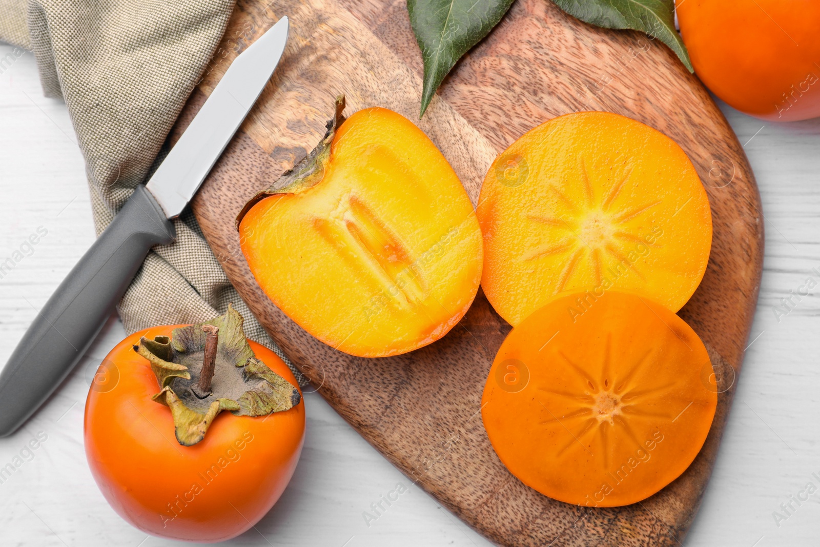 Photo of Delicious ripe juicy persimmons and knife on white wooden table, flat lay