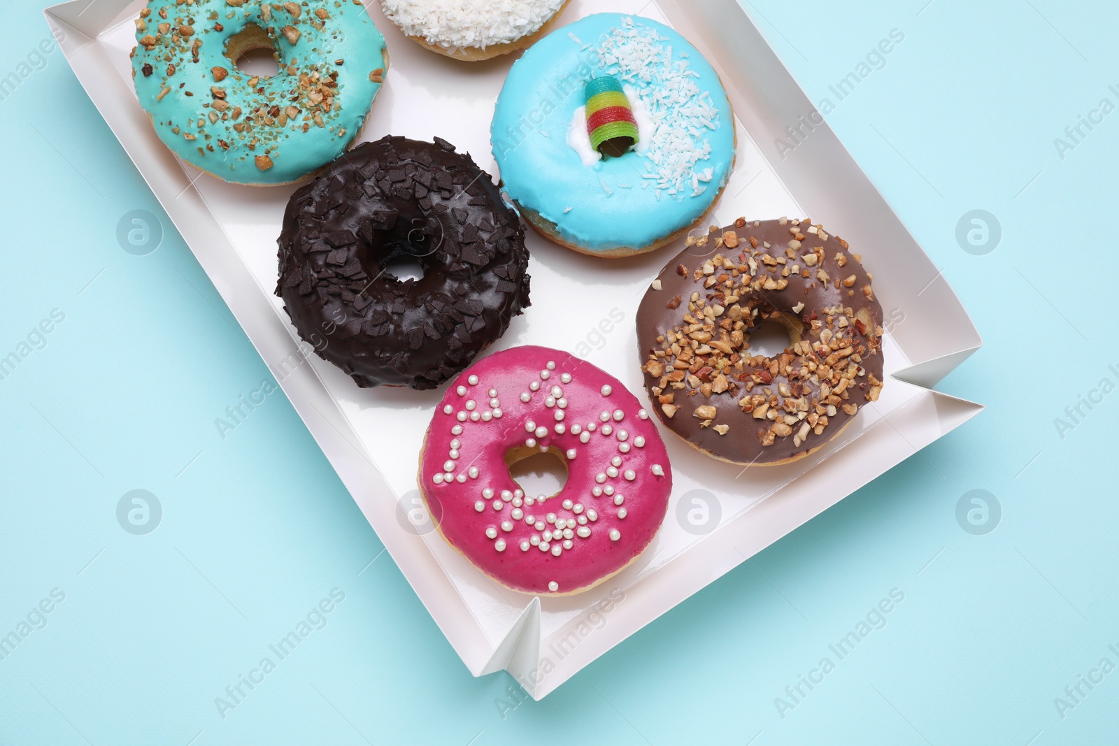 Photo of Box with different tasty glazed donuts on light blue background, top view