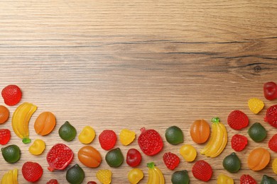Photo of Delicious gummy fruit shaped candies on wooden table, flat lay. Space for text