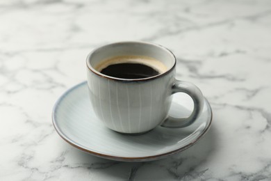Photo of Tasty coffee in cup and saucer on white marble table, closeup