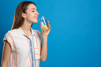 Photo of Young woman drinking lemon water on light blue background. Space for text