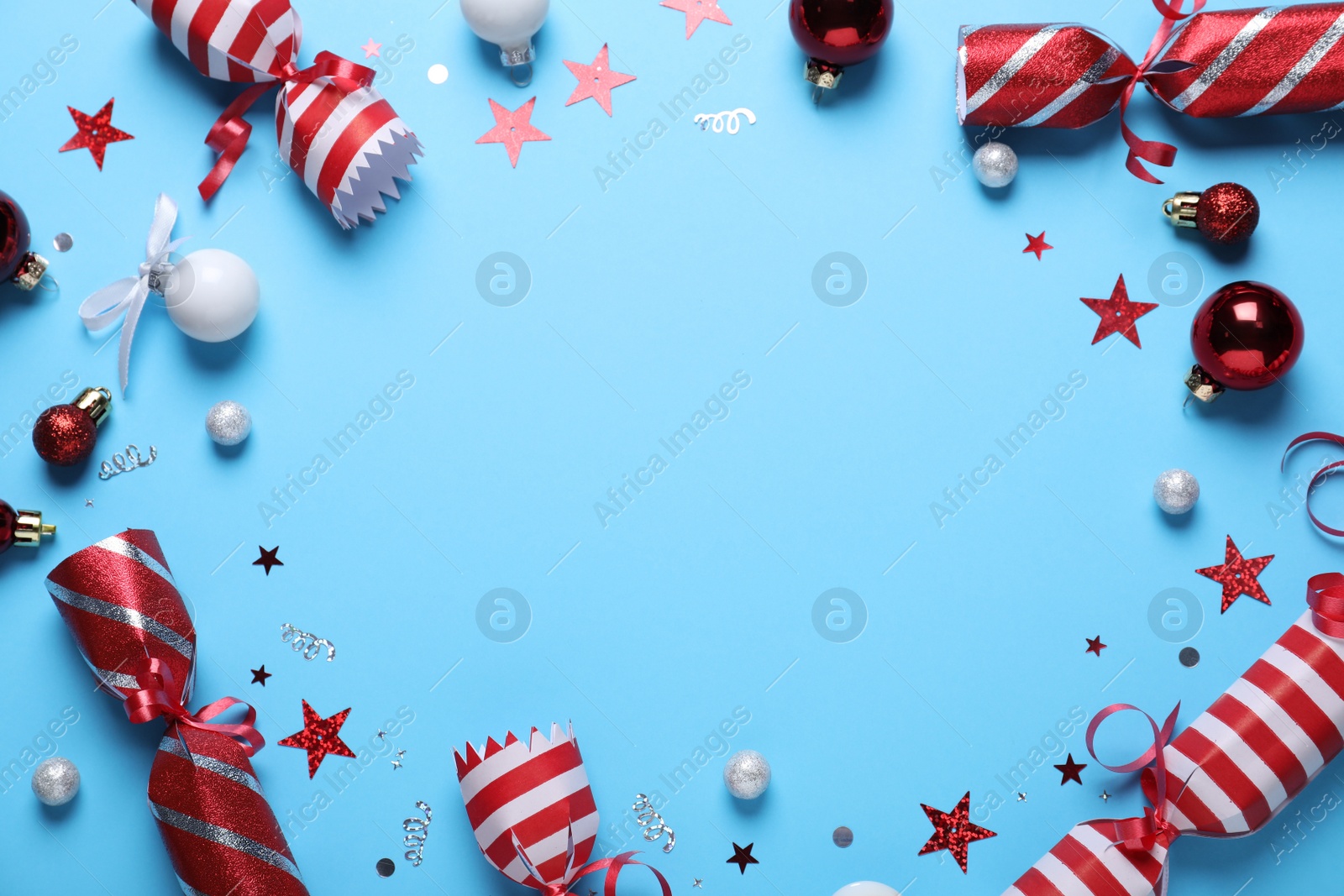 Photo of Frame of Christmas crackers and decorations on light blue background, top view with space for text