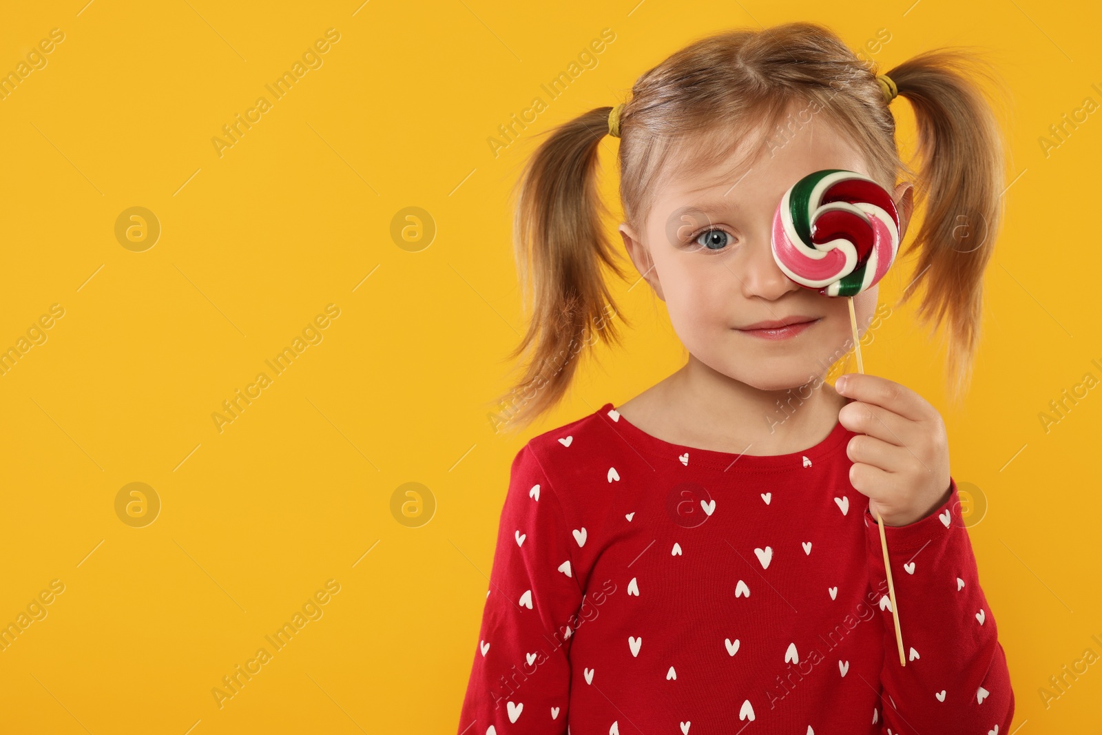 Photo of Cute girl covering eye with lollipop on orange background, space for text