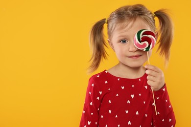 Photo of Cute girl covering eye with lollipop on orange background, space for text