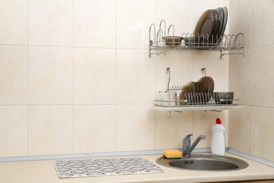 Photo of Clean dishware on drying rack over sink in kitchen, space for text