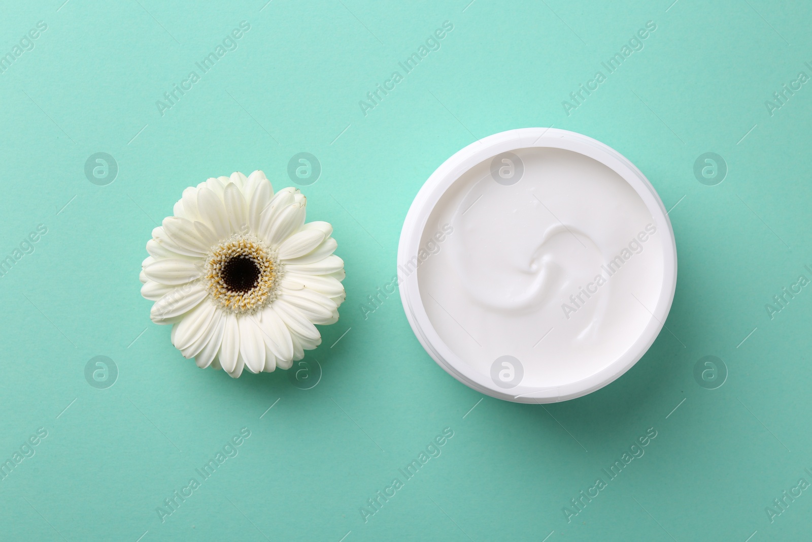 Photo of Moisturizing cream in open jar and gerbera flower on turquoise background, flat lay. Body care product