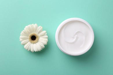 Moisturizing cream in open jar and gerbera flower on turquoise background, flat lay. Body care product