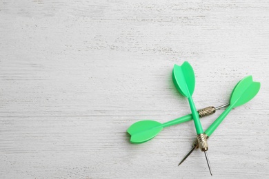 Photo of Green dart arrows on white wooden table, flat lay with space for text