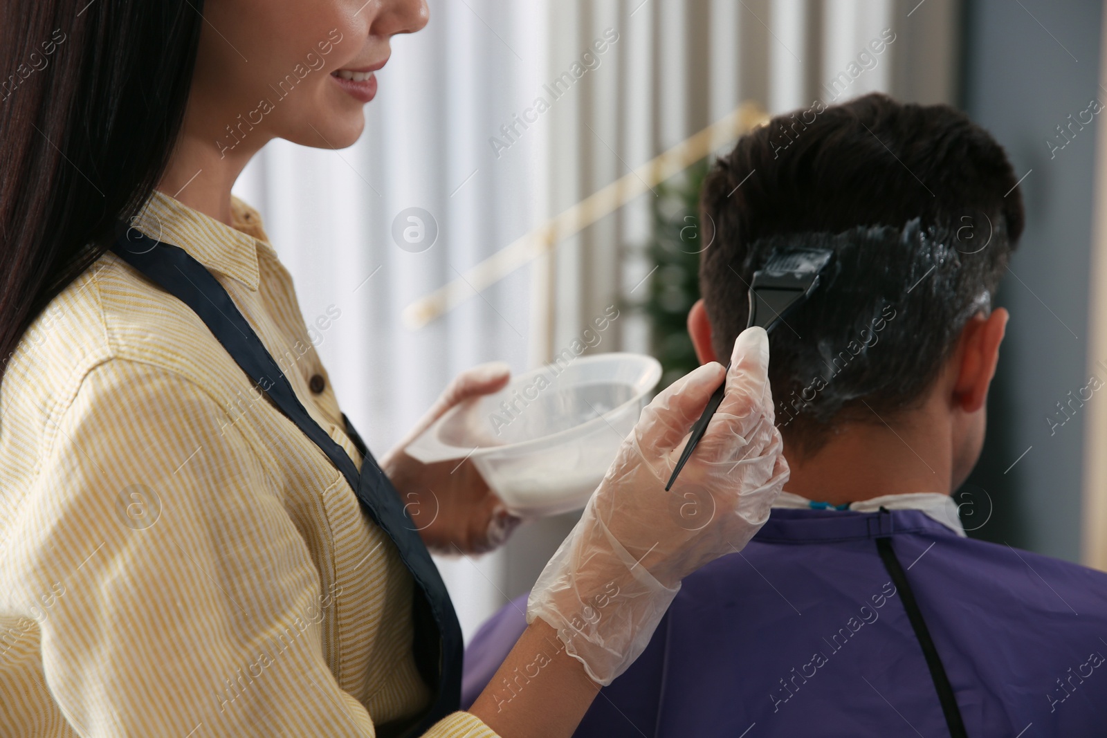 Photo of Professional hairdresser dying hair in beauty salon, closeup