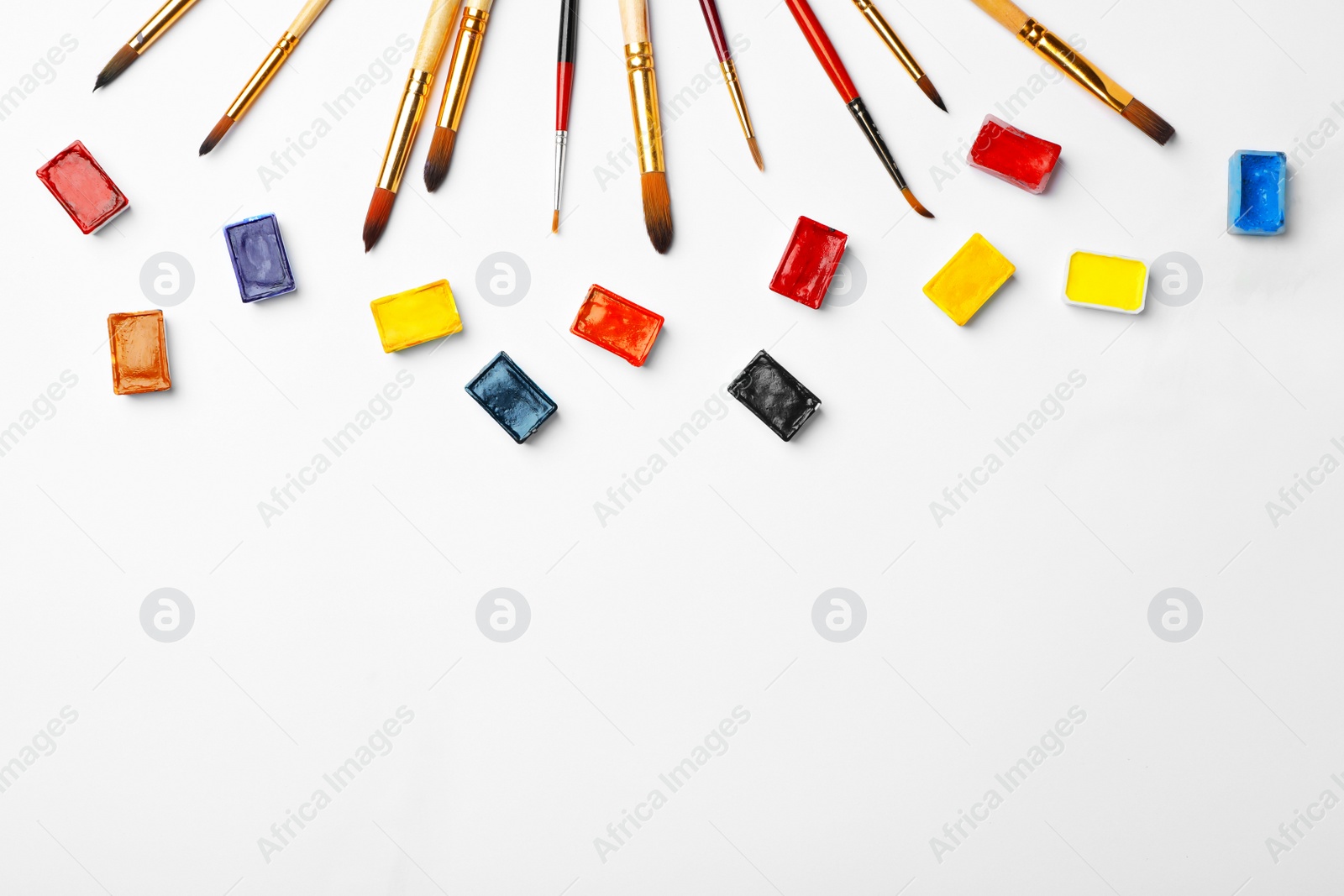 Photo of Colorful paints in pans for palette tray and brushes on white background, top view