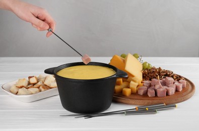 Photo of Woman dipping piece of ham into fondue pot with tasty melted cheese at white wooden table, closeup
