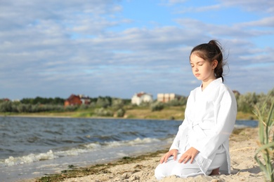 Cute little girl in kimono meditating near river. Karate practicing
