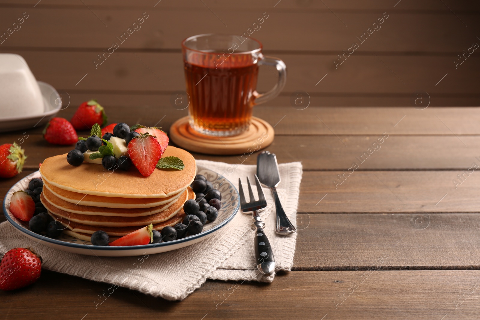 Photo of Delicious pancakes with fresh berries and butter served on wooden table, space for text